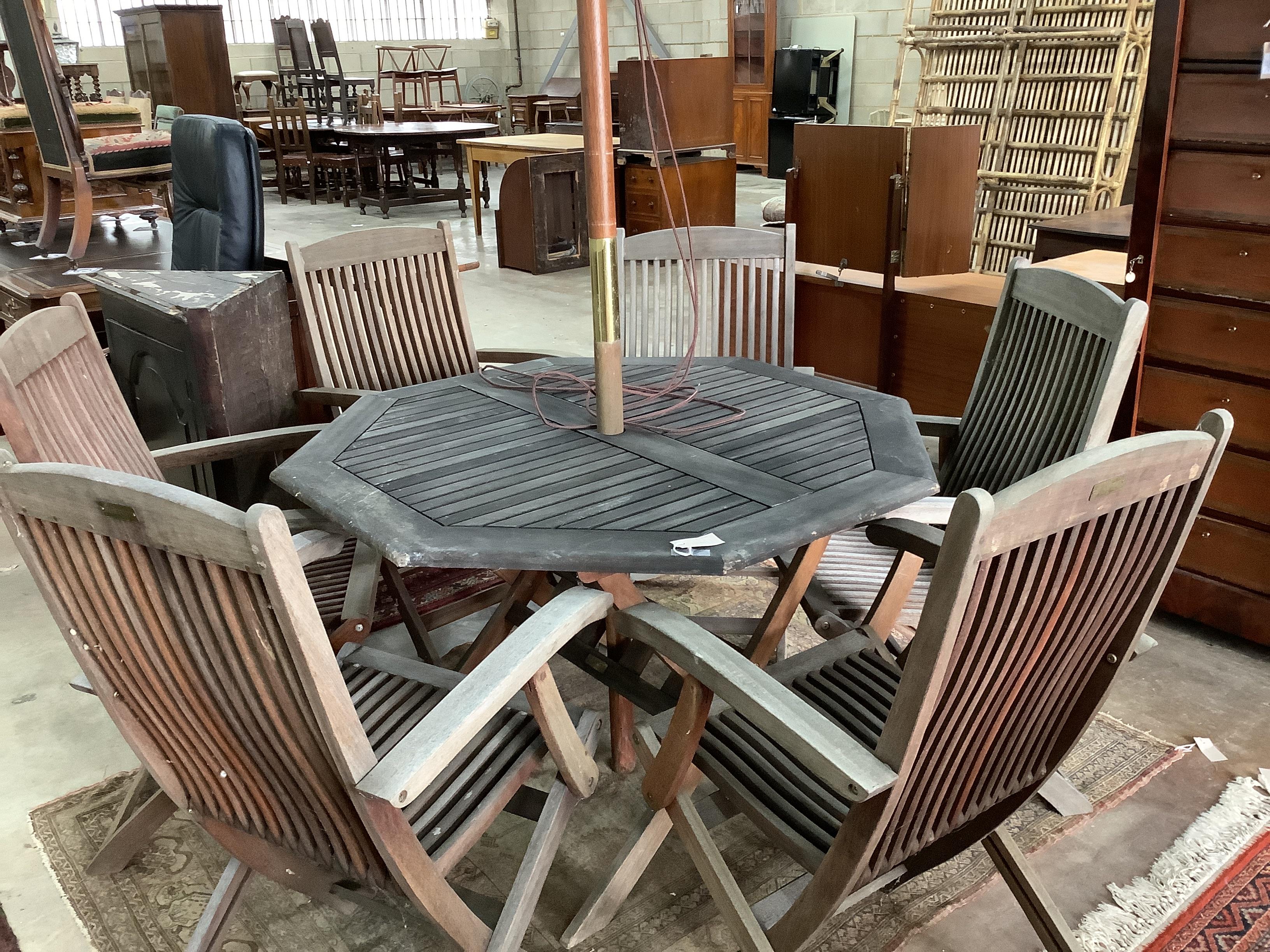 A weathered teak octagonal garden table, width 112cm, height 72cm together with six Beaufort weathered teak folding garden elbow chairs and green canvas crank parasol
